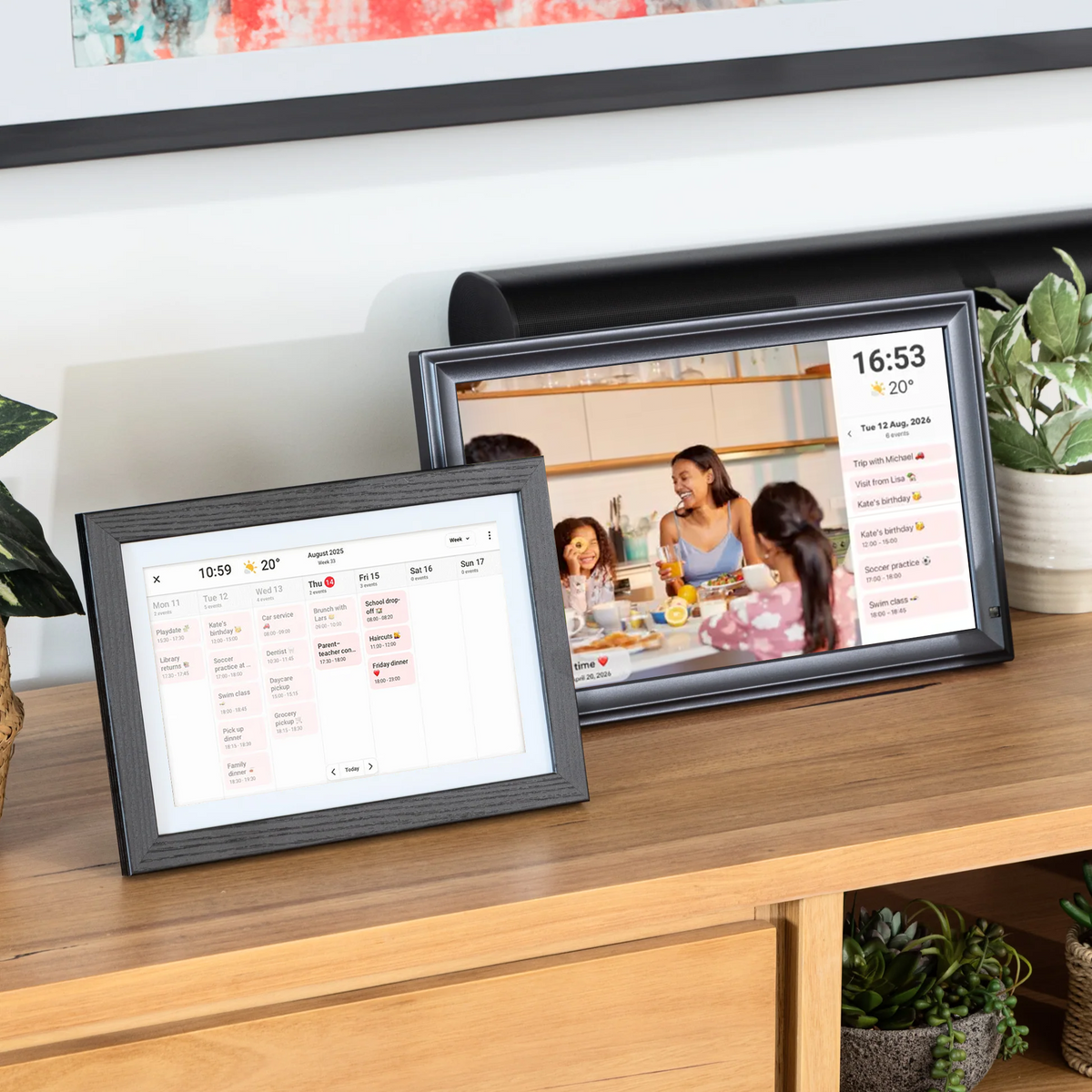 Two LuvLink digital calendars displayed on a wooden shelf showing calendar and photo views with plants nearby.