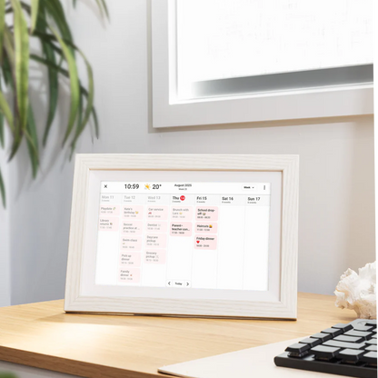 LuvLink digital calendar displaying August 2025 schedule on wooden desk with plant and keyboard nearby.