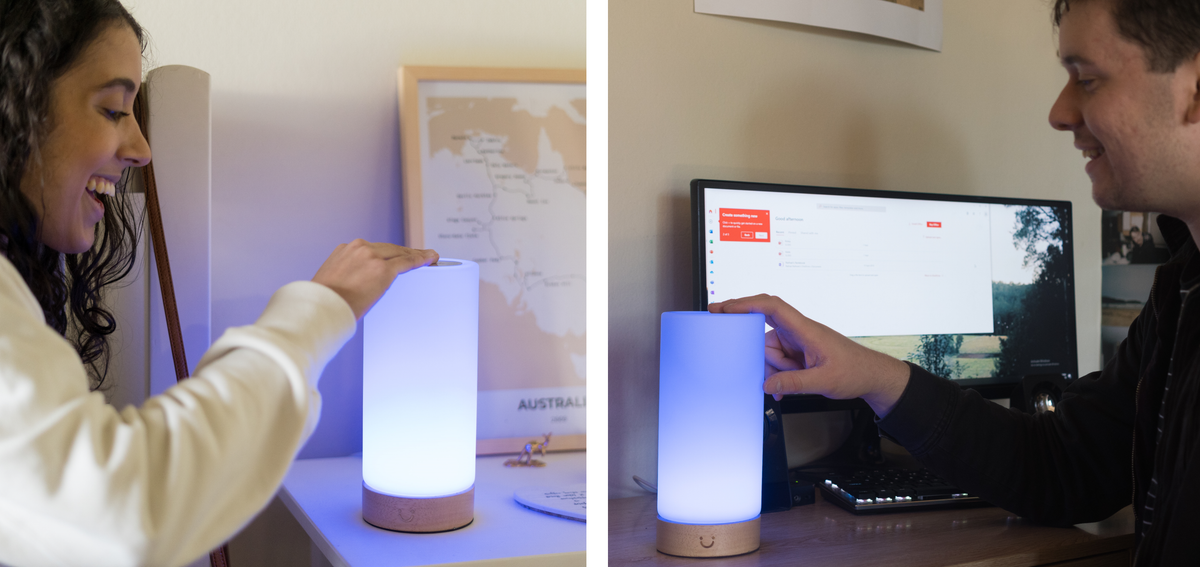 Couple touches and admires the soft blue glow of a cylinder lamp across two separate home spaces.