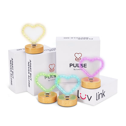 Pulse friendship lamps in warm white, green, blue and pink neon hearts on wooden bases surround branded packaging.