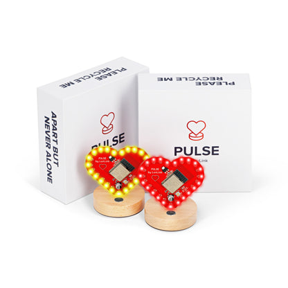 Pulse friendship lamps glow with red and gold LED hearts on wooden stands beside their branded boxes.