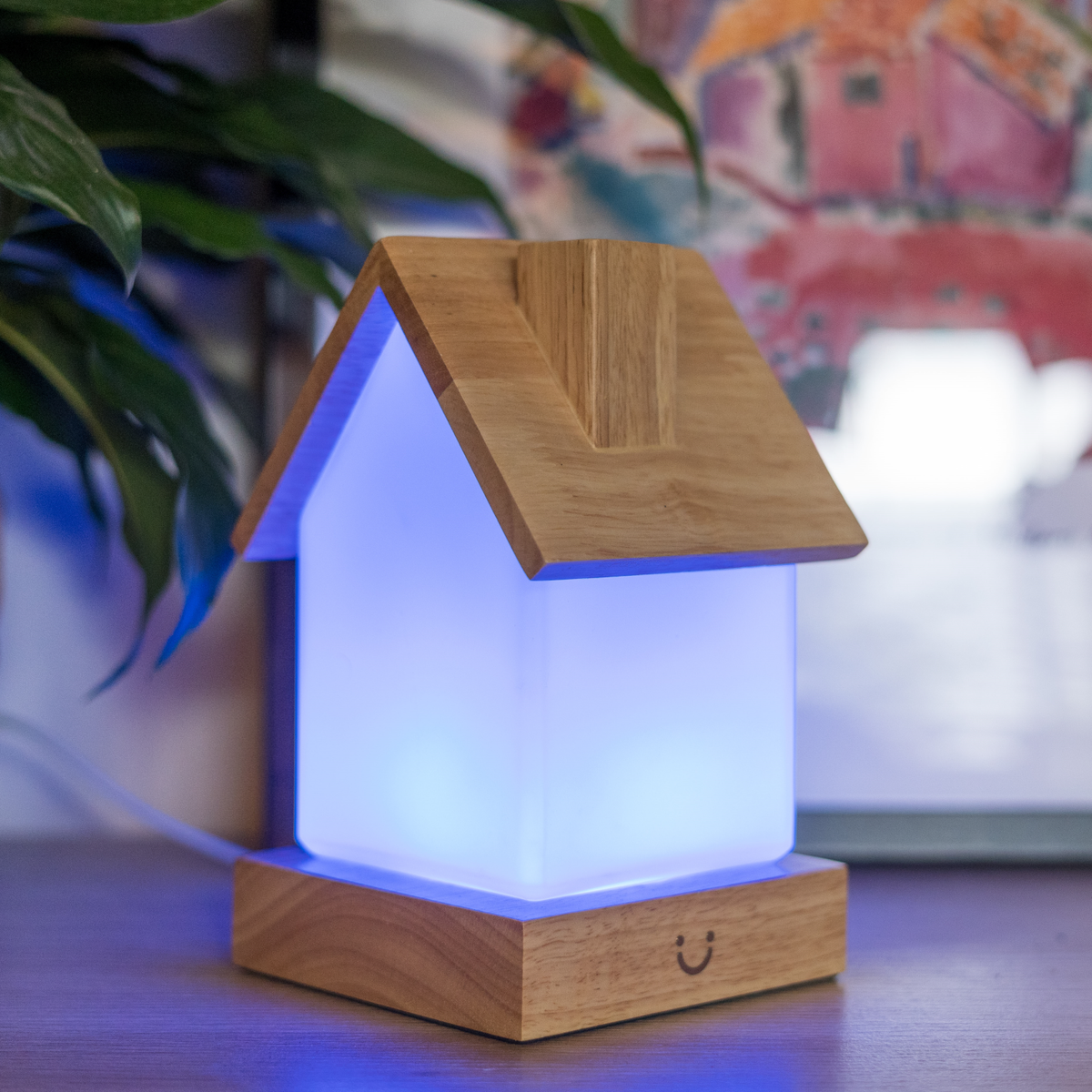 House-shaped lamp glows with soft blue light, wooden roof and base with cheerful smiley face.