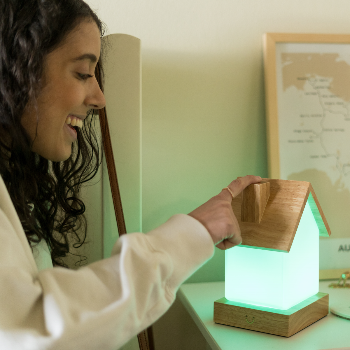 A person lifts the wooden roof off a glowing house-shaped lamp emitting soft green light.