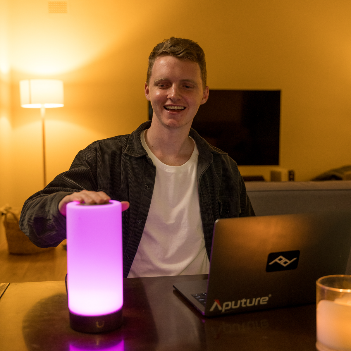 Smiling man showcases a vibrant magenta Modern Cylinder Lamp at his desk.