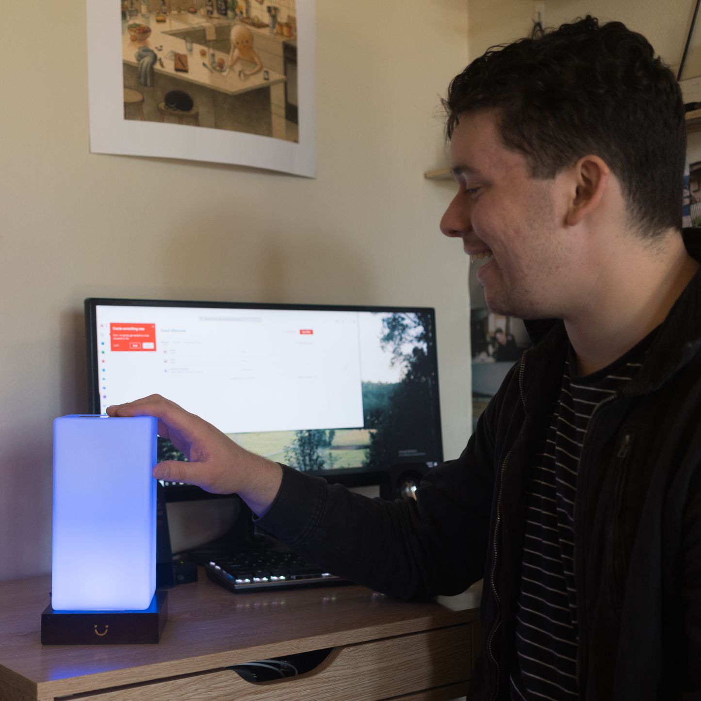Person touching a glowing blue tower lamp while working at a desk setup.