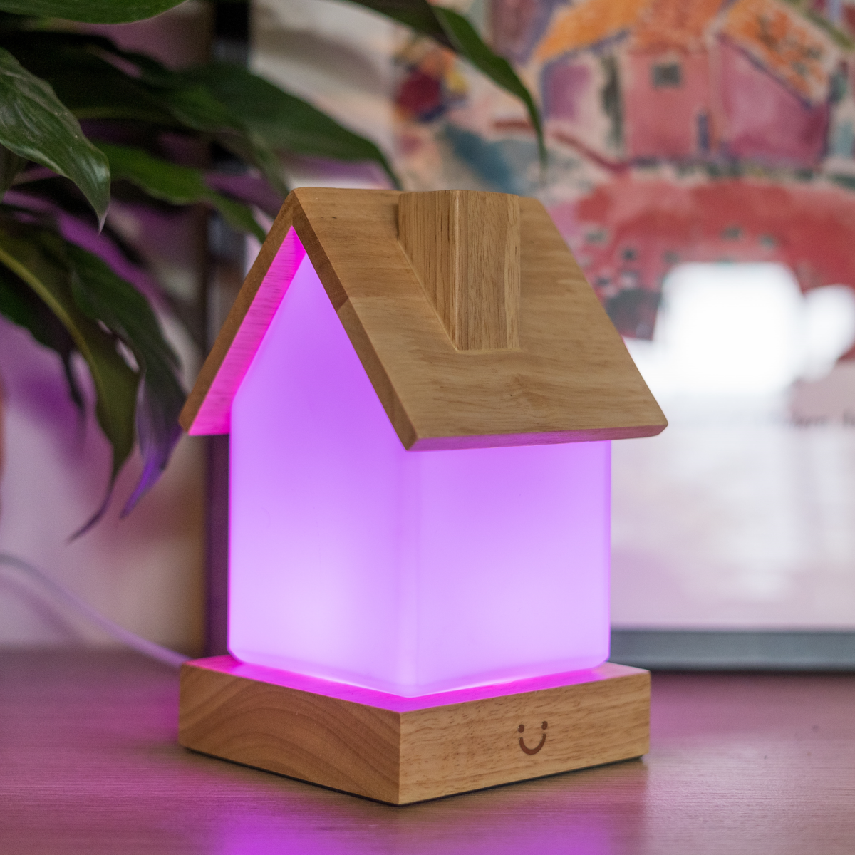 Vibrant magenta light glows from a lamp with timber roof and base beside leafy plant décor.