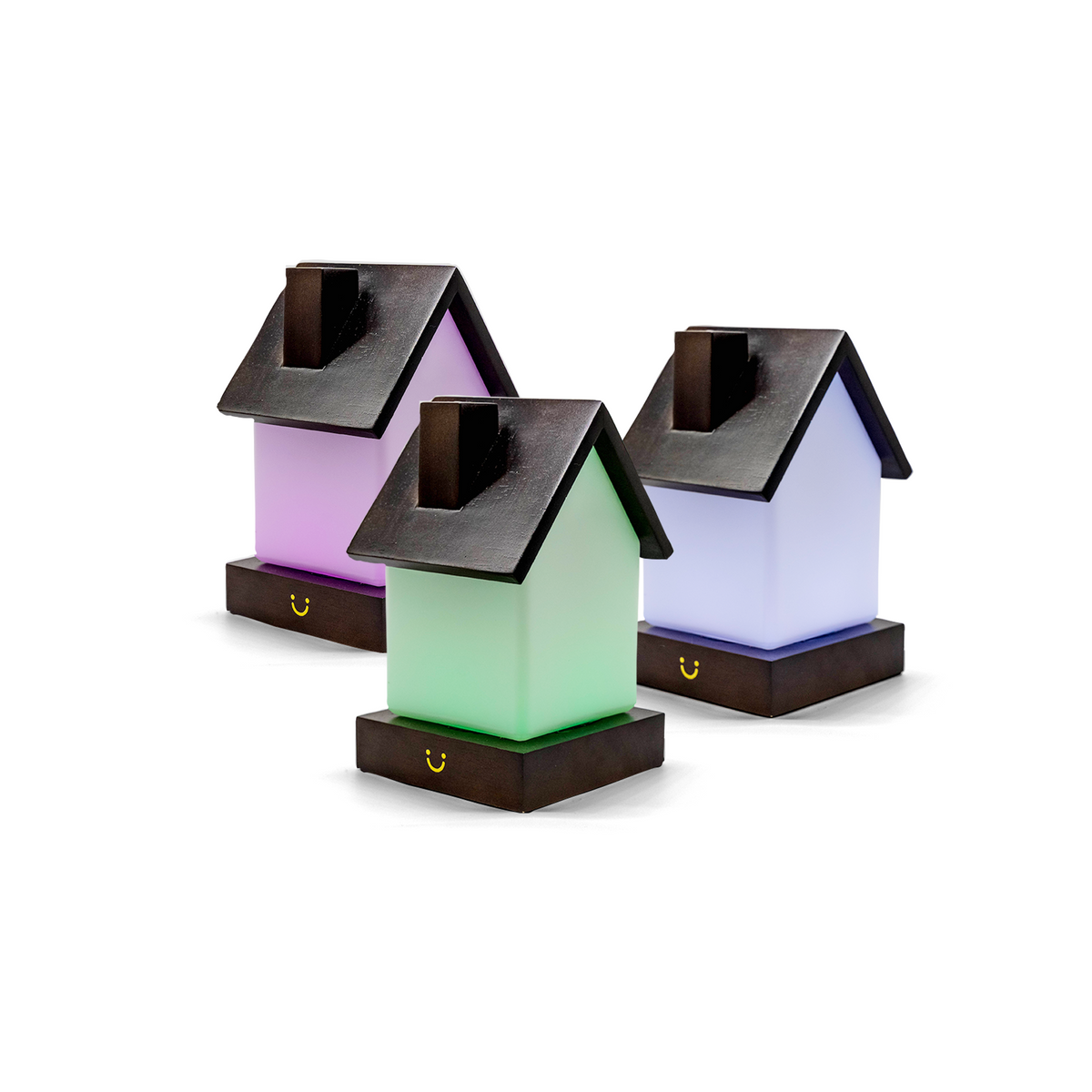 Pink, green and lavender house-shaped lamps glow with dark roofs and wooden bases displayed side by side.