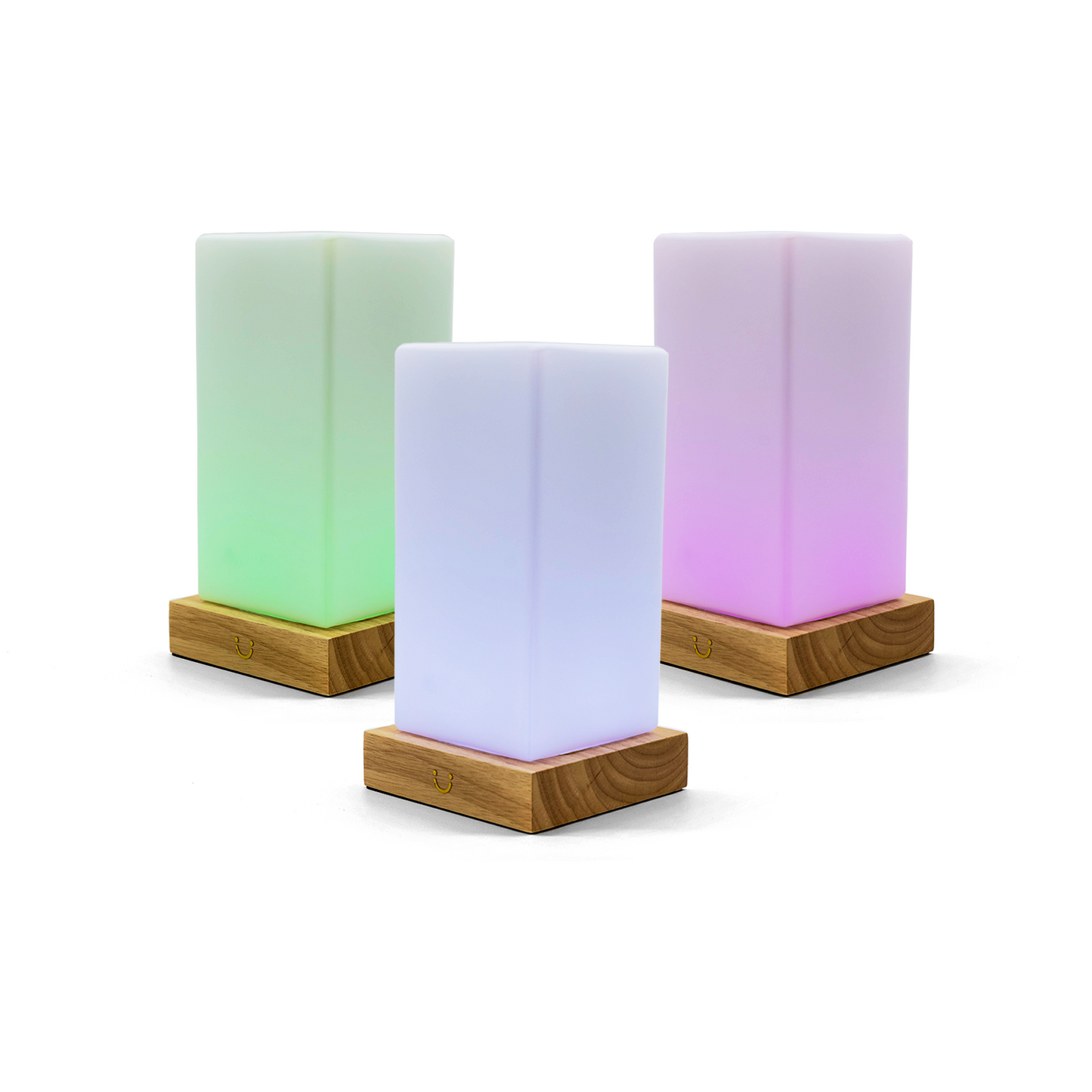 Glowing friendship lamps in green, blue and pink sit on wooden bases against a white background.
